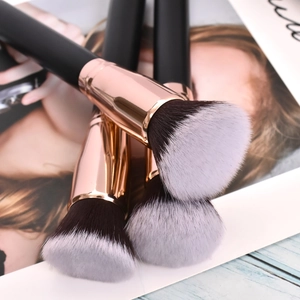 Close-up of three makeup brushes with black handles and rose gold ferrules on a magazine