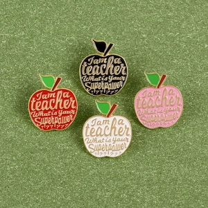 Detail of four colorful apple enamel pins with teacher superpower slogan on green grass
