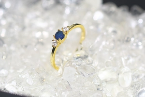 Macro shot of gold wedding ring with blue sapphire and zircon stones on white pebbles