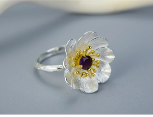 Macro view of silver floral ring with gold stamen and a purple gemstone center