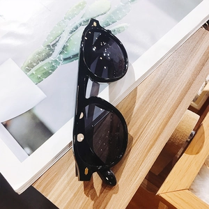 Detailed close-up of oversized black sunglasses with gold metal trim on a wooden table