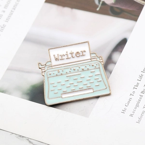 Mint green typewriter enamel pin with Writer text on a magazine background