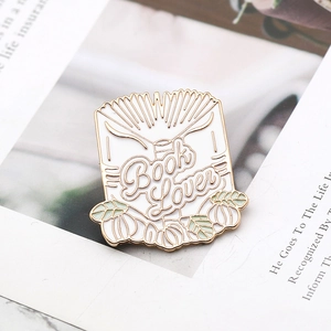 White enamel book lover brooch with gold metal outline and green leaf decorations