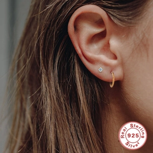 Detail of 925 sterling silver zircon stud and twisted gold hoop earring set on ear