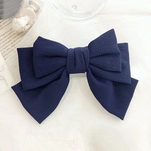 Macro detail of navy blue triple-layered oversized bow hair clip on textured fabric