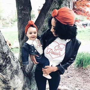 Detail showing mother and infant wearing matching orange donut knot turban headwraps
