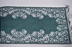 Detailed view of dark green scarf with white floral lace trim and black fringe tassels