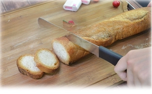 Gros plan d'un couteau à pain en acier inoxydable coupant une baguette sur une planche