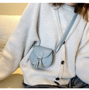 Detail showing a light blue mini saddle bag with tassels on a child's shoulder