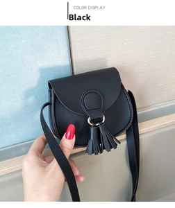 Close-up of black mini saddle bag with tassel detail and sleek crossbody strap