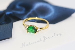 Macro view of three-stone gold ring with oval green emerald and zircon accents