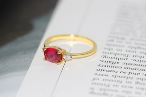 Macro shot of gold plated oval red zircon ring with side stones on a book page