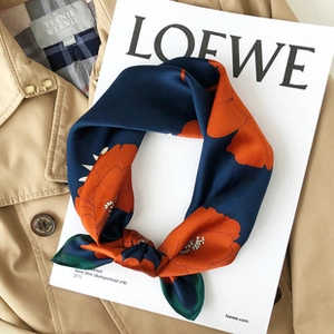 Detail of silk scarf with orange floral pattern on navy blue silk folded on classic trench coat