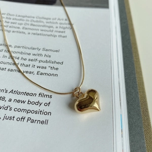 Macro view of a 3D gold heart pendant on a polished snake bone chain necklace