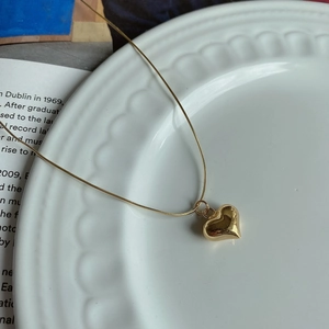 Detailed close-up of a gold heart pendant on a fine snake chain over a textured ceramic dish