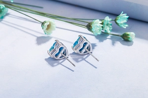 Close-up of heart-shaped blue opal stud earrings with cubic zirconia on floral surface