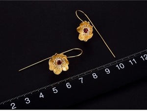 Close-up of golden floral earring with garnet gemstone and ruler measurement scale