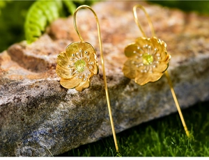 Macro shot of gold floral earrings with green gemstones on a natural gray stone background