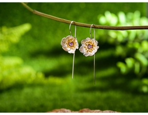 Macro detail of silver flower earrings with purple gemstone on natural mossy branch