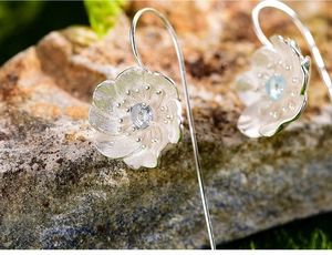 Macro shot of silver flower earrings with gemstones on natural rock texture