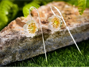 Detail of silver floral earrings with olive green gemstone and gold pistil on mossy rock