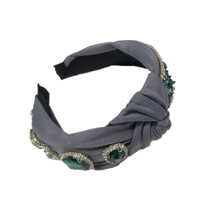 Baroque retro knotted headband with emerald gemstones on gray fabric, studio shot