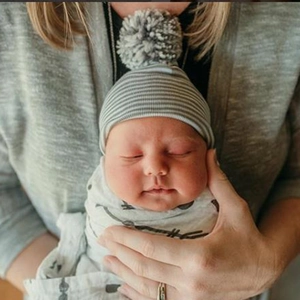 Newborn baby wearing a grey and white striped knitted beanie with a large pom-pom detail