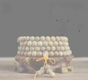 Detailed close-up of 108 wood prayer beads with yellow tassel on a vintage wooden base