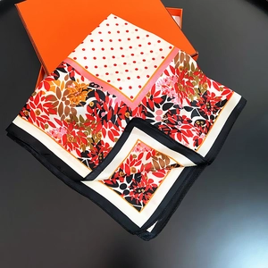 Détail d'un carré de soie avec motifs floraux à côté d'une boîte cadeau orange de luxe
