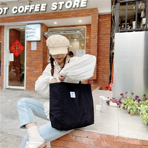 Detailed view of a black canvas tote bag with white square label used by a model