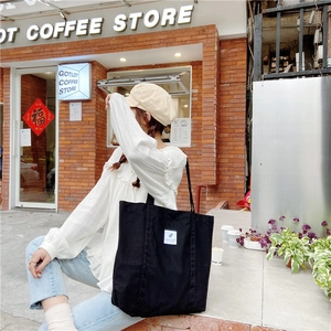 Detail shot of a black corduroy tote bag with white label on casual model outfit
