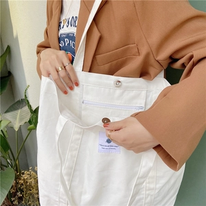 Detail of white canvas tote bag featuring front zipper pocket and metal snap button closure