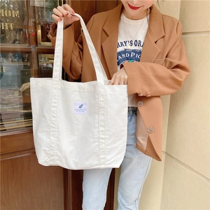 Minimalist white canvas tote bag with leaf label shown on a model in street style