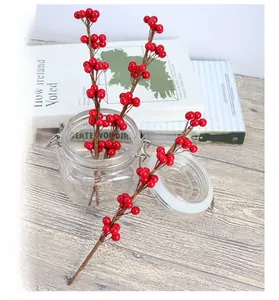 Dettaglio di bacche rosse artificiali in un vaso di vetro su sfondo di legno naturale