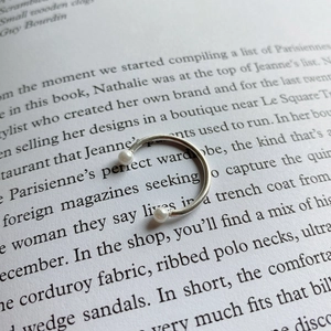 Close-up of S925 sterling silver open ring featuring elegant pearls on vintage book page