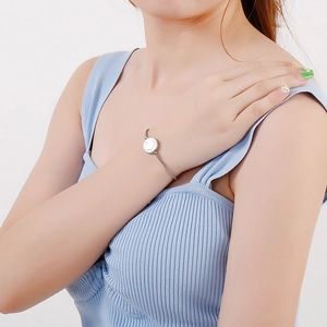 Minimalist silver stainless steel bangle with white circular charm on model's wrist