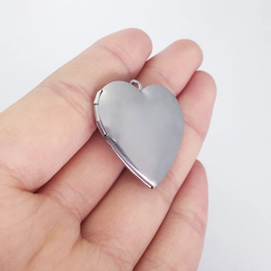Polished silver heart-shaped locket pendant held in hand for scale and detail