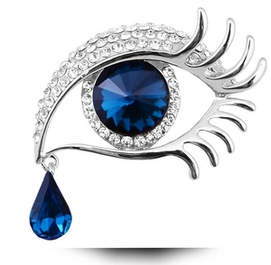 Macro shot of silver eye brooch with blue crystal teardrop and sparkling pavé eyelashes