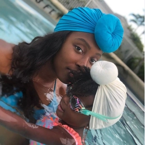 Lifestyle detail of mother and child wearing matching donut style turban hats in a pool