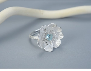 Macro detail of silver flower ring featuring a matte finish and light blue gemstone