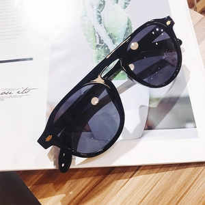 Detailed view of oversized black sunglasses with gold metal accents on stylish wood grain