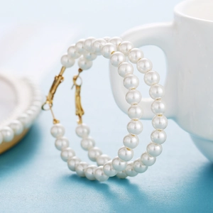 Close-up of large gold hoop earrings with white faux pearls on a light blue background