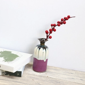 Artistic purple and white glazed ceramic vase with red berry stems on a wooden table