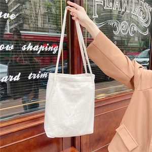 Close-up of a white washed cotton canvas tote bag carried by a hand in a street setting
