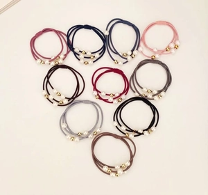 Detailed view of ten colorful elastic hair ties with pearls and golden beads on beige base