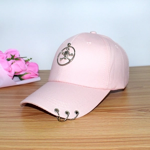 Pink baseball cap featuring metal skull ring and side hoop accents on a wooden table
