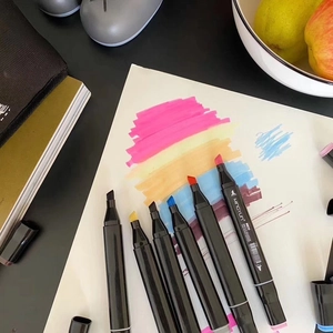 Flat lay of open double-tipped art markers showing vibrant ink colors on a dark desk