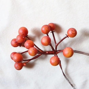 Artificial orange-red holly berry branch for home decor on a soft white plush background