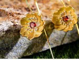 Macro detail of gold flower earrings with natural red garnet and matte petals
