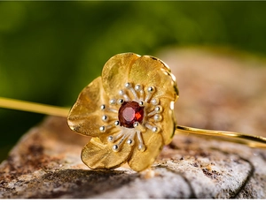 Detailed macro view of gold flower earrings featuring a red gemstone and silver stamen
